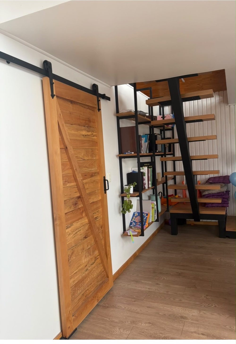 Puerta corrediza de madera con herrajes negros y escalera al fondo